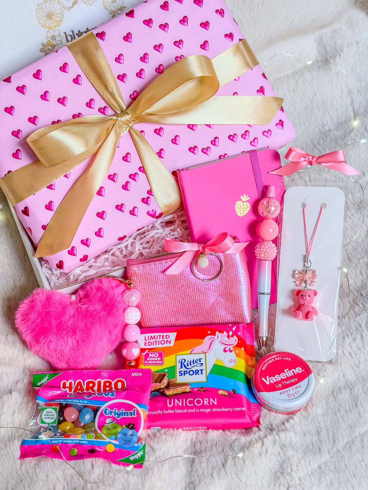 Pink Girly Box avec paquet rose à cœurs, ruban doré, Bag charm, phone charm et stylo assemblés par Bloomlov accessoires assortis, chocolat licorne et bonbons