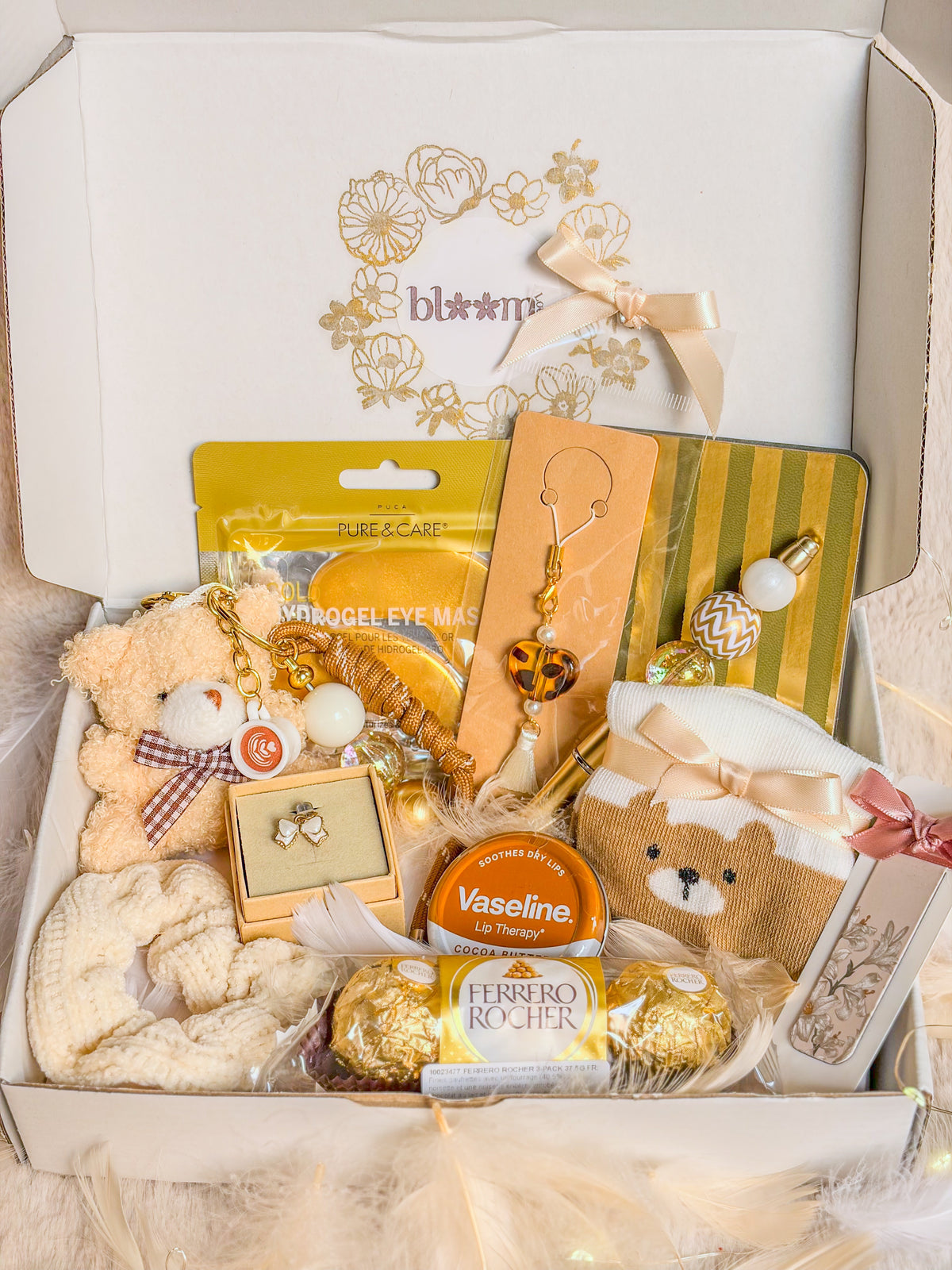 Bear Cozy Box BloomLov ouverte avec son assortiment de cadeaux dans les tons crème et dorés


