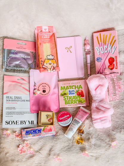 Contenu de la Pinky Self-Care Box BloomLov disposé à plat : Phone charm, Dust Plug ou bouchon anti-poussière et stylo assemblés par nos soins, soins de beauté, accessoires roses, carnet et gourmandises