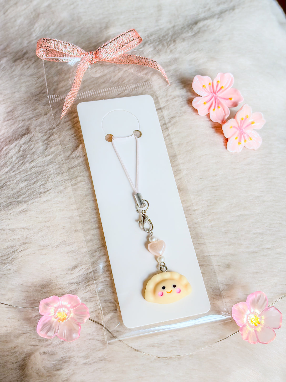 Phone charm dumpling BloomLov avec ravioli souriant, perle cœur rose pâle et attache blanche sur carte