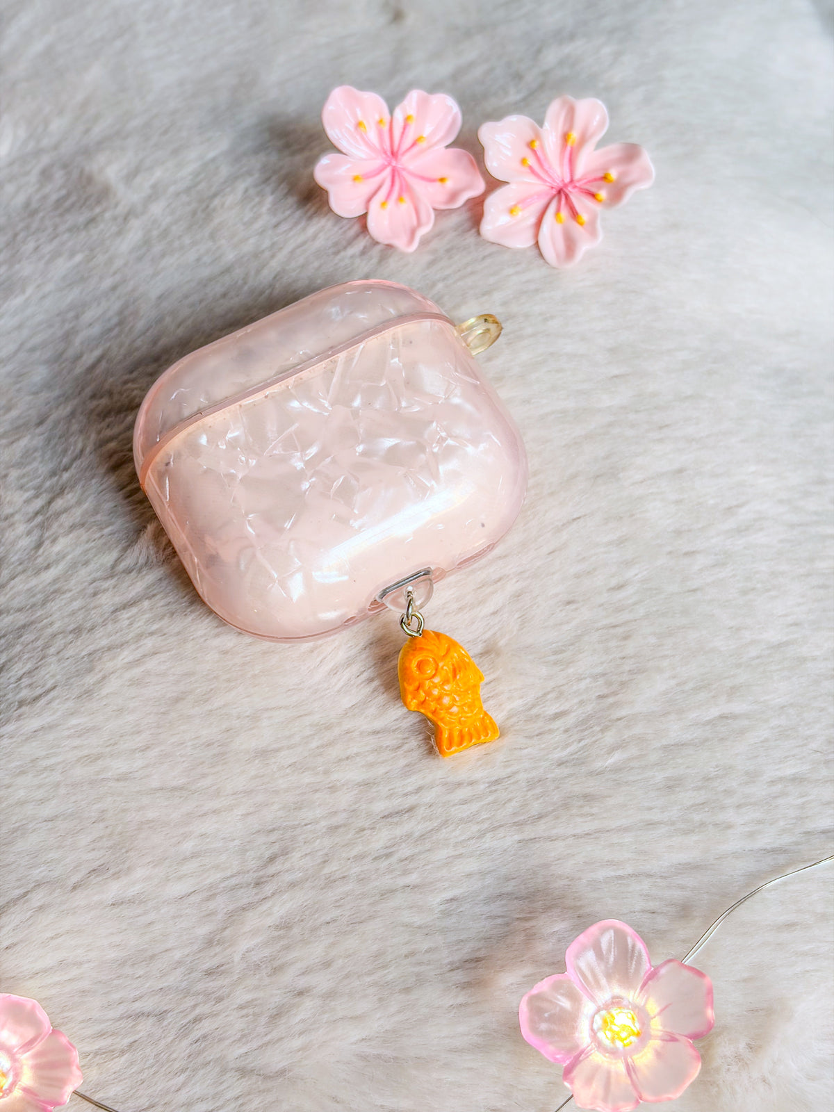 Bouchon anti-poussière taiyaki BloomLov présenté sur un boîtier d’écouteurs avec coque rose nacrée
