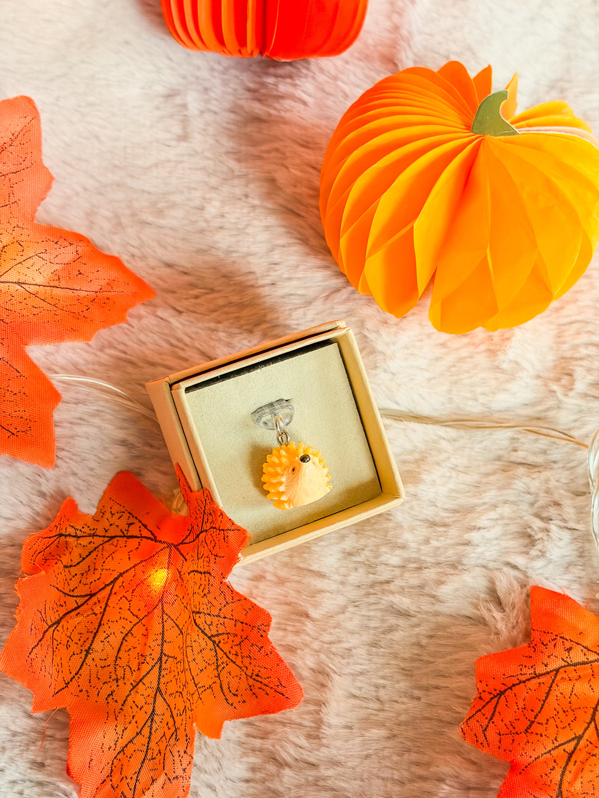 Bouchon anti-poussière hérisson BloomLov jaune et crème dans son écrin, entouré de feuilles d’automne