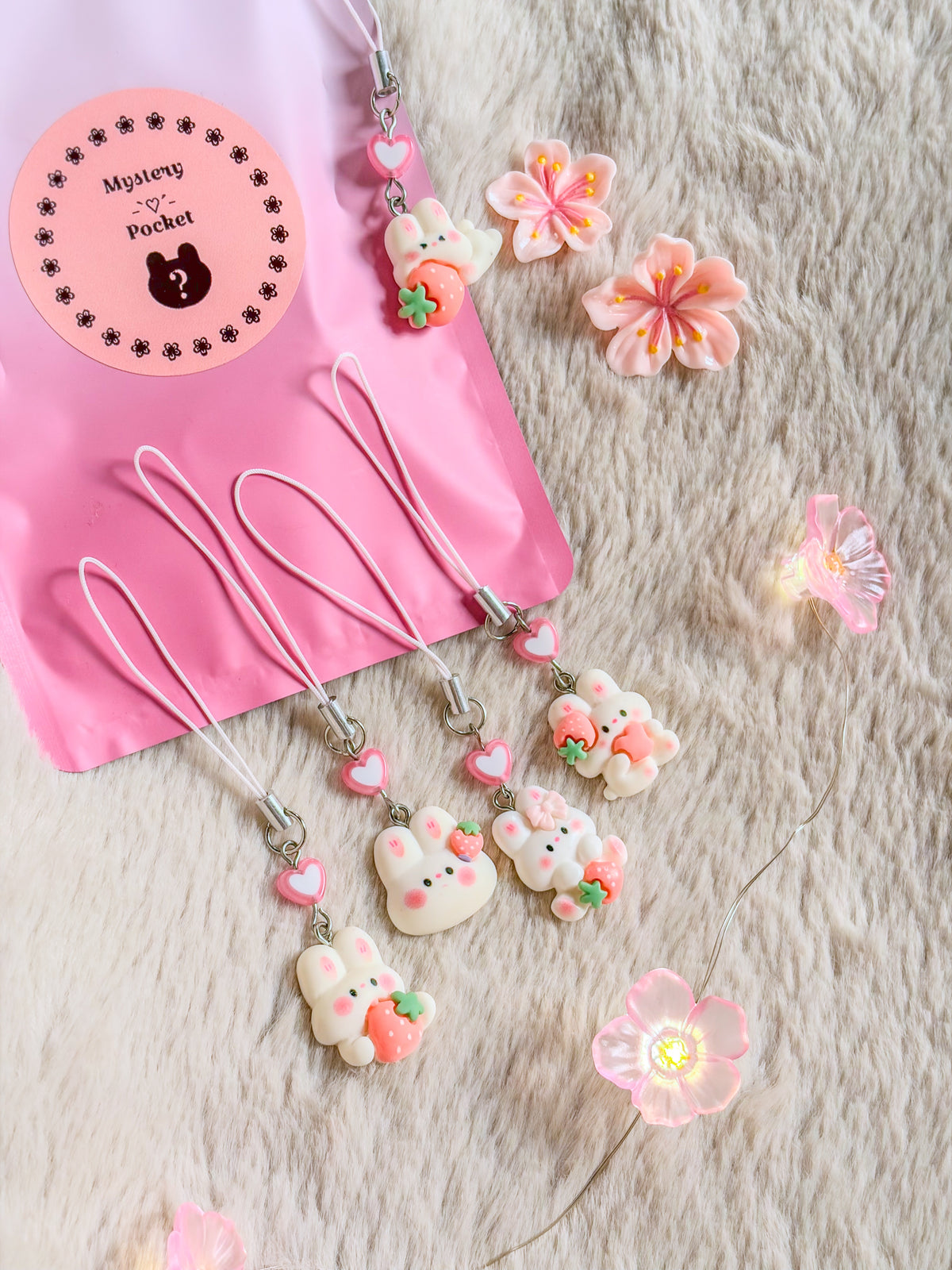 Exemples de phone charms lapin et fraise BloomLov avec perles cœur, devant leur pochette Mystery Pocket