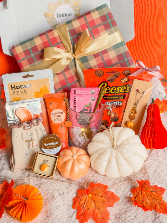 Coffret cadeau d’automne BloomLov avec soins, tasse, gourmandises et accessoires devant un paquet à ruban doré.