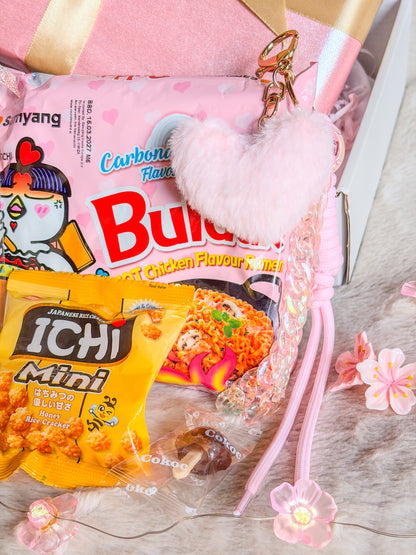 Bag charm cœur rose avec chaîne et cordon devant les Buldak Carbonara et les crackers ICHI Mini


