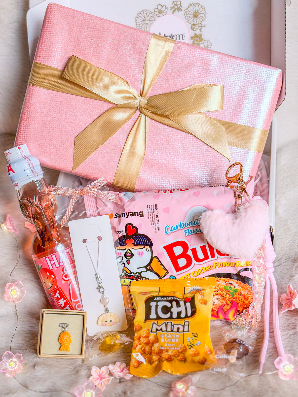 Box cadeau asiatique kawaii BloomLov avec Buldak Carbonara, Ramune fraise, snacks et accessoires devant un paquet rose

