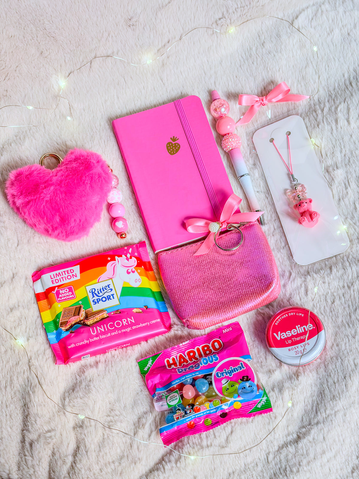 Contenu de la Pink Girly Box BloomLov à plat : accessoires roses, carnet, soin lèvres, chocolat et bonbons

