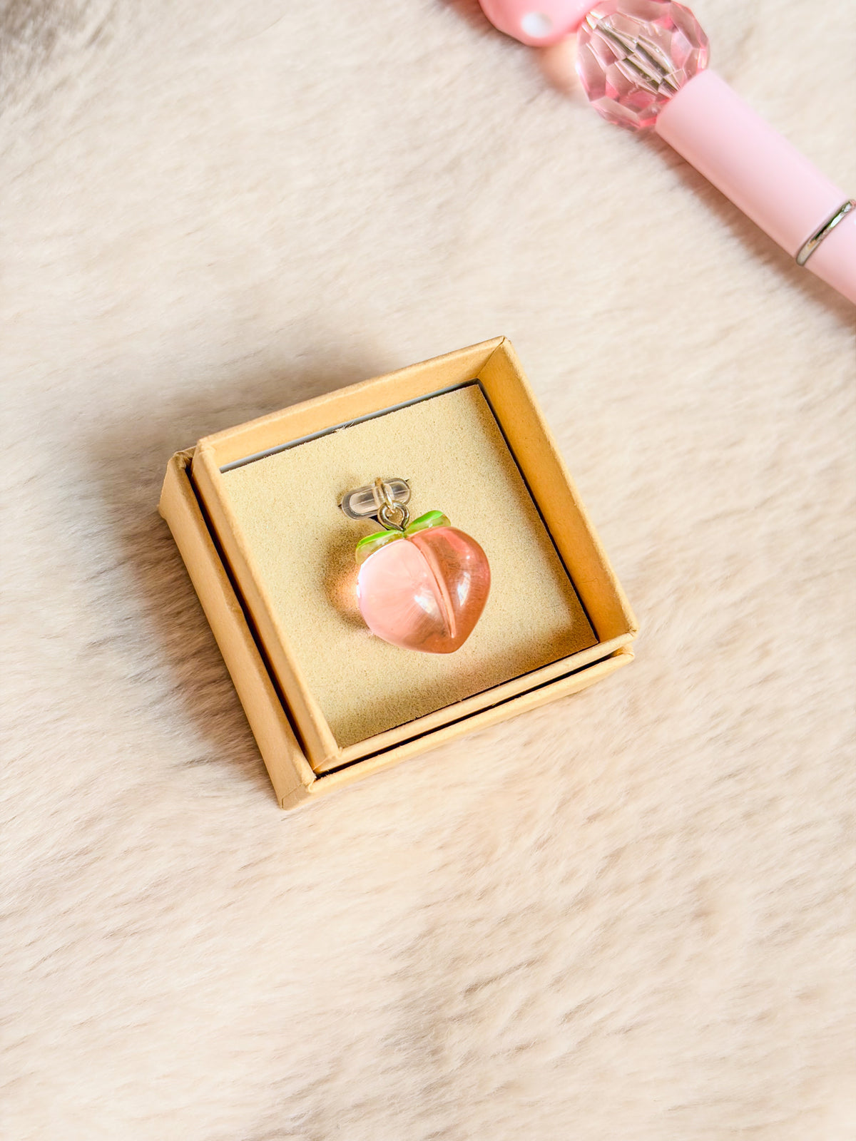 Bouchon anti-poussière pêche BloomLov rose translucide avec feuilles vertes, présenté dans son écrin