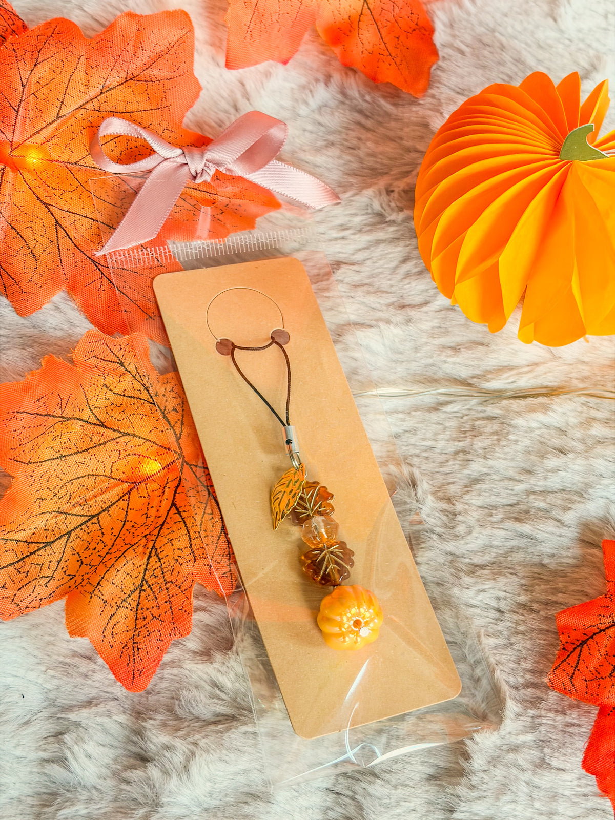 Phone charm BloomLov avec citrouille orange, perles ambrées et feuilles dorées, présenté sur carte