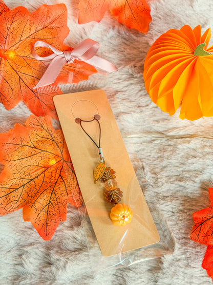 Phone charm BloomLov avec citrouille orange, perles ambrées et feuilles dorées, présenté sur carte