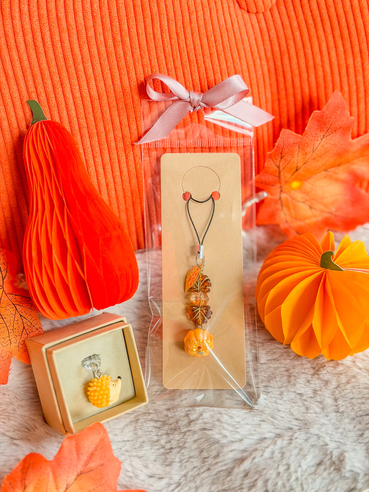 Phone charm citrouille et bouchon anti-poussière hérisson BloomLov présentés parmi des décorations d’automne

